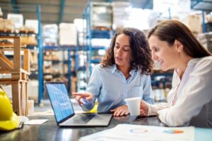 Woman showing inventory on laptop to warehouse manager